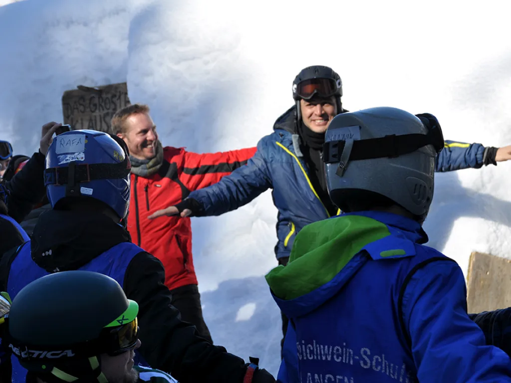 Zwei Personen zeigen den Jugendlichen etwas an der Hütte.